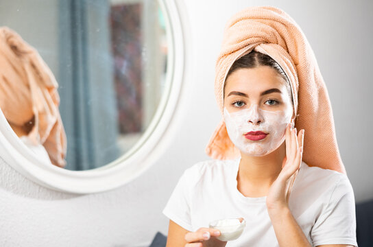 Happy woman taking care of face skin with the lotion