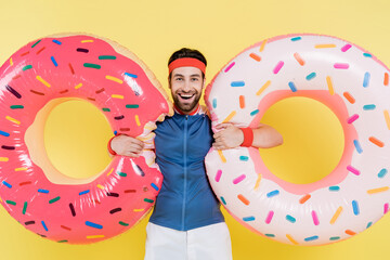 Smiling sportsman holding swim rings isolated on yellow.