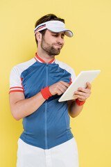 Skeptical sportsman using digital tablet isolated on yellow.