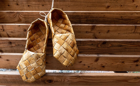 Birchen woven bast shoes hang on a log wall.