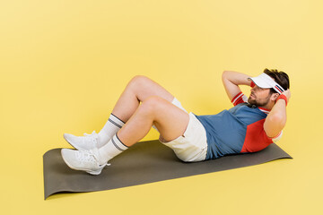 Bearded sportsman doing abs on fitness mat on yellow background.