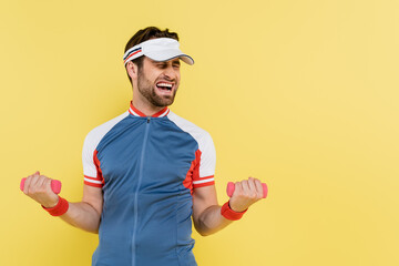 Sportsman in visor training with dumbbells isolated on yellow.