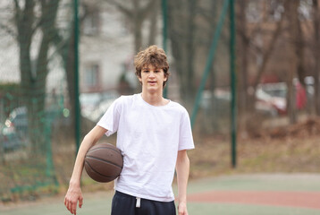 Cute young teenager in white t shirt with a ball plays basketball. Sports, hobby, active lifestyle for boys
