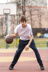 Cute young teenager in white t shirt with a ball plays basketball. Sports, hobby, active lifestyle for boys