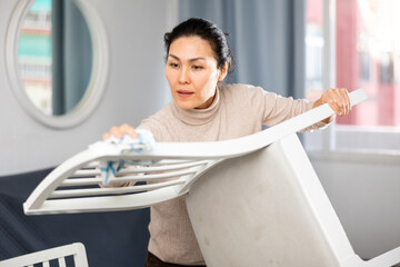 Concentrated asian woman cleaning up the apartment wipes a chair with a damp cloth