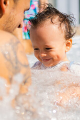 young dad with his latin baby boy with funny hairstyle, wet from pool. matroswimming activity. vertical picture