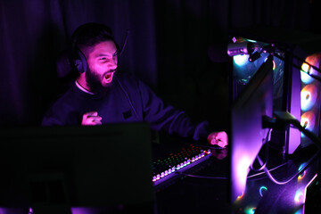 Fototapeta na wymiar young man playing computer games at home neon beam studio man wearing headphones having fun playing games on the internet