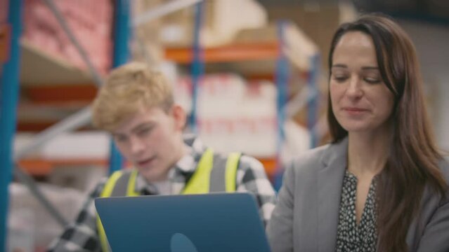 Female manager training male intern sitting at laptop in busy distribution warehouse - shot in slow motion