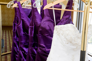 Wedding dress and purple bridrsmaid dresses hanging on a bell cart