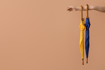 Female hand with umbrellas in colors of Ukrainian flag on brown background