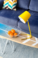 Surfboard with stylish lamp and oranges near sofa in interior of living room