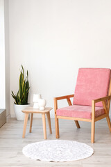 Stylish pink armchair and table with vases in interior of room
