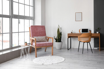 Stylish pink armchair and table with computer in interior of room