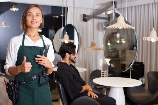 positive woman hairdresser thumbs up and man visitor in salon.
