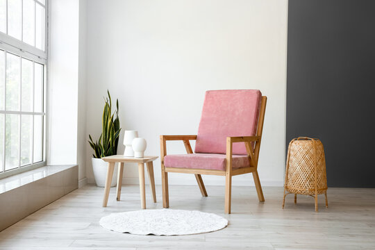 Stylish pink armchair and table with wicker lamp in interior of room