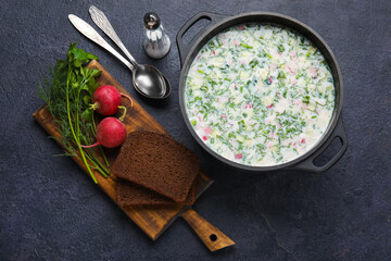 Composition with cooking pot of tasty okroshka and ingredients on dark background