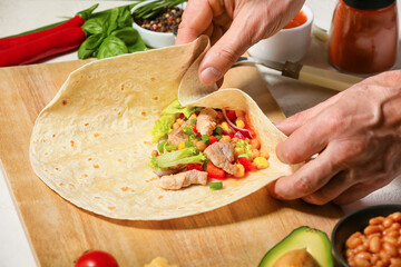 Man preparing tasty burrito with meat on table