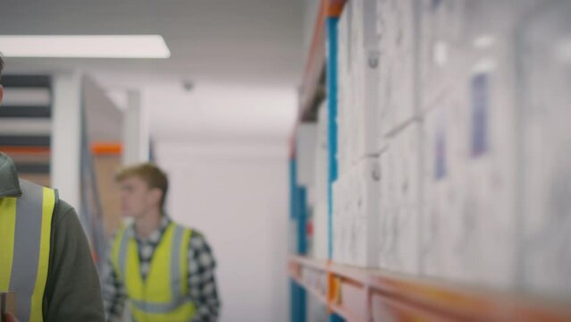 Camera tracks past warehouse shelves to show male worker in distribution warehouse wearing PPE face mask and looking into camera - shot in slow motion