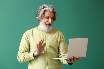 Bearded senior man video chatting with laptop on green background