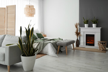 Interior of stylish bedroom with fireplace, soft bench and houseplant