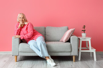 Mature woman sitting on sofa near pink wall