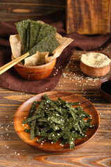 Plate and bowl of tasty seaweed sheets with sesame on wooden background © Pixel-Shot
