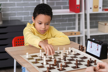 Little African-American boy playing chess during tournament in club