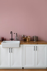 Counters with sink, kitchen utensils and food near pink wall