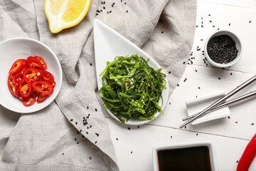 Plate with healthy seaweed salad and ingredients on light wooden background © Pixel-Shot