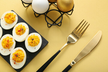Board and holder with stuffed eggs on yellow background. Easter celebration