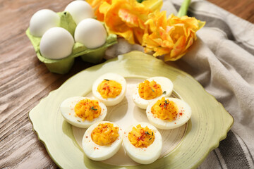 Plate with stuffed eggs, flowers and napkin on wooden background. Easter celebration