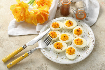 Plate with stuffed eggs, flowers, cutlery and spices on light background. Easter celebration