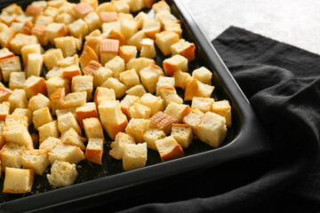 Baking dish with tasty croutons and napkin on light background, closeup