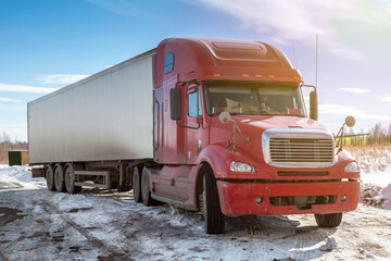 Red long-distance bonnet truck with a white semitrailer in the countryside at winter