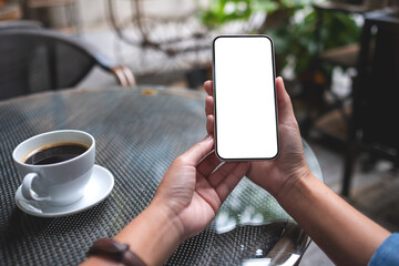 Mockup image of a woman holding mobile phone with blank desktop screen in cafe