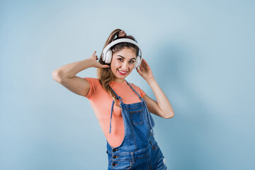 hispanic young woman with headphones, dancing and listening music on blue background in Mexico Latin America	