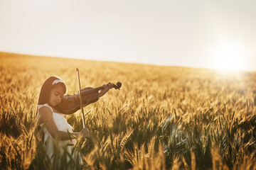 Giving the crops a little musical encouragement. Shot of a cute little girl playing the violin...