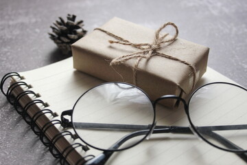 Blank Notebook, Pen, Glasses and small gift boxes placed on a gray table.