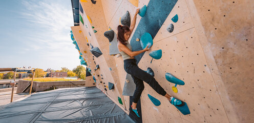 Bouldering climbing athlete woman training strength at outdoor gym boulder climb wall. Asian fit girl going up having fun in extreme sport hobby. Banner panoramic - obrazy, fototapety, plakaty