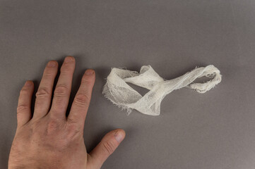 The hand of a mature man and a piece of white bandage against a gray background. Health and...