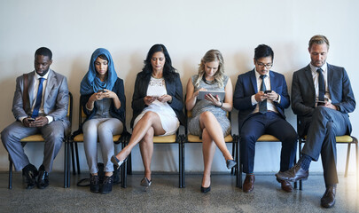 Staying connected while they wait. Shot of a group of well-dressed businesspeople using their smartphones while waiting to be interviewed.
