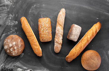 Fresh bread on a black background, top view. Homemade fresh pastries of various loaves of wheat and rye bread close-up.