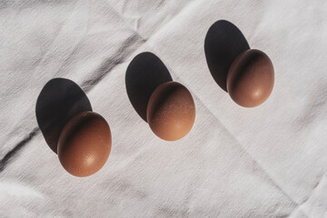 Three eggs on linen fabric with sun shadows.