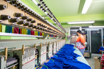 A worker stands in control of a sewing machine. Embroidery area in textile factory in industrial...