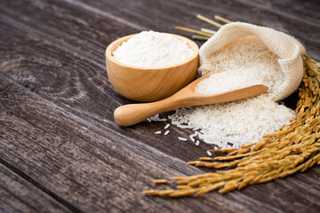 White jasmine rice and white rice powder in wooden bowl with paddy isolated on rustic wooden table background.