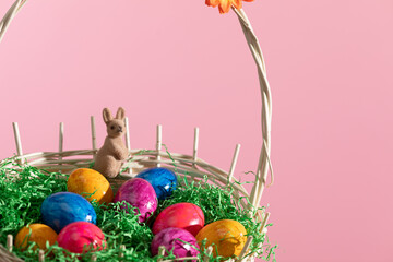 Easter basket with Easter eggs and a brown bunny on a pink background.