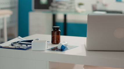 No people in examination cabinet with x ray scan and bottle of pills on desk, medical space prepared for checkup appointment. Empty office with equipment and intruments. Close up.