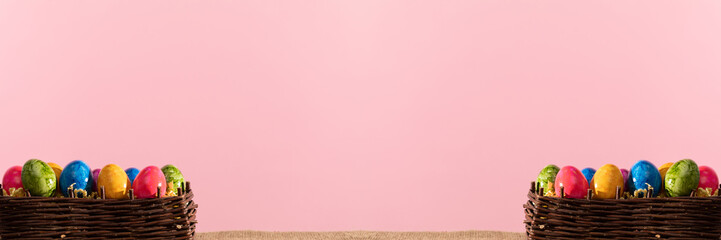 Panoramic shot of basket full of Easter eggs on pink solid background. Easter.
