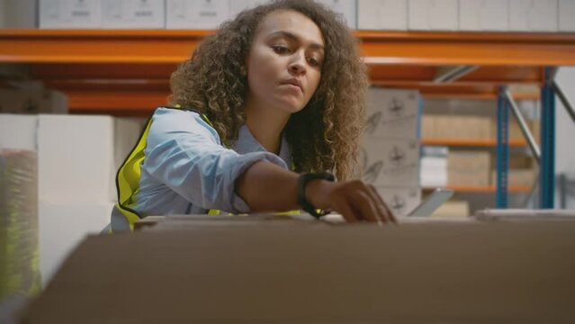 Female worker with digital tablet in distribution warehouse checking barcode information on box on shelf - shot in slow motion
