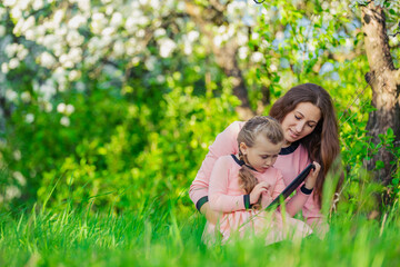 Fototapeta premium mother, with her daughter looking at the tablet on the background of flowering trees